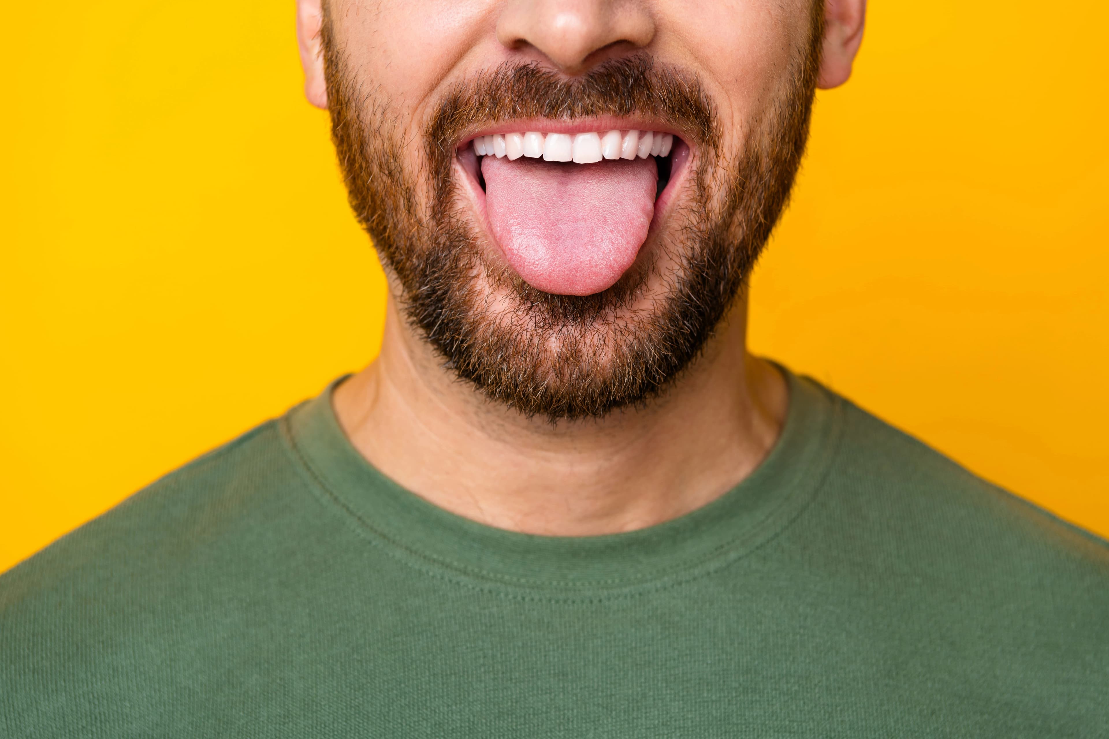 Smiling bearded man sticking his tongue out against a bright yellow background