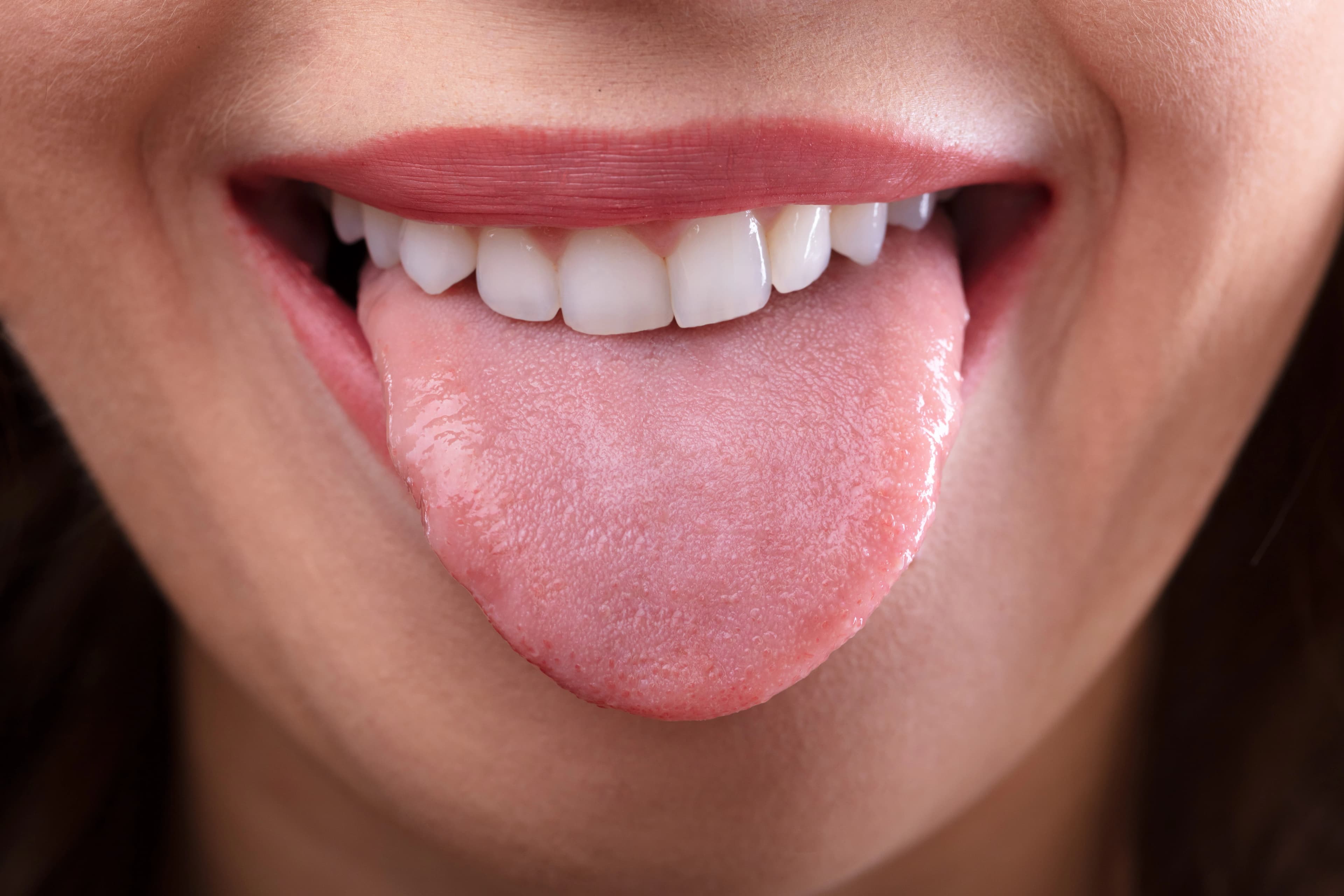 Close-up of a person's mouth with a healthy pink tongue extended and clean white teeth